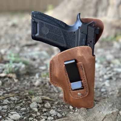 Brown leather IWB holster with clip holding compact pistol in outdoor setting
