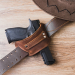 Brown leather belt slide holster mounted on a leather belt, showing open-top design and reinforced stitching for secure everyday carry